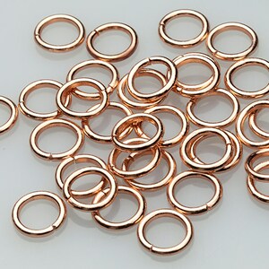 May include: A pile of small, rose gold jump rings. The rings are all the same size and are arranged in a random pattern.