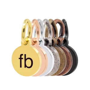 Op de afbeelding: Een set van zeven ronde metalen bedels met een lus aan de bovenkant. De bedels zijn in verschillende afwerkingen: goud, rosé goud, zilver, antiek messing, koper en zwart. De gouden bedel heeft de letters "fb" gegraveerd.