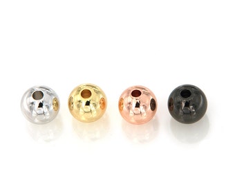May include: Four round metal beads with a textured surface. The beads are silver, gold, rose gold, and black.