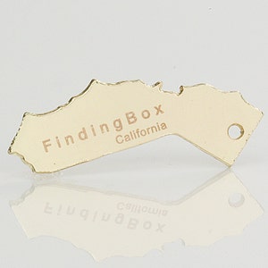 Puede incluir: Encanto de metal de color dorado con forma del estado de California con el texto "FindingBox California" en &eacute;l.
