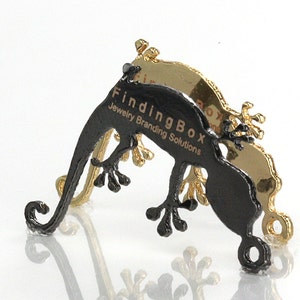 Puede incluir: Expositor de joyer&iacute;a en forma de gecko negro con el texto "FindingBox Jewelry Branding Solutions" impreso en el lateral. El expositor est&aacute; hecho de metal y tiene un acabado dorado.