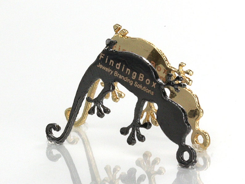 Puede incluir: Expositor de joyer&iacute;a en forma de gecko negro con el texto "FindingBox Jewelry Branding Solutions" impreso en el lateral. El expositor est&aacute; hecho de metal y tiene un acabado dorado.