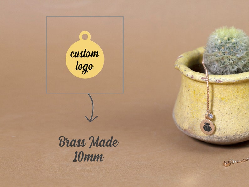 May include: A gold-colored brass tag with a round shape and a hole at the top. The tag is 10mm in diameter and has the text "custom logo" printed on it. The tag is shown next to a small potted cactus.