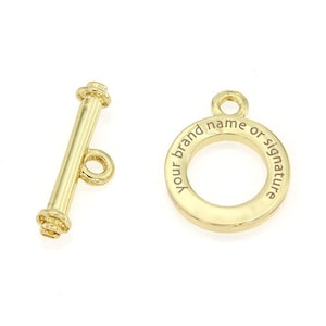 Op de afbeelding: Gouden metalen toggle sluiting met een ronde ring waarop "Your brand name or signature" staat.