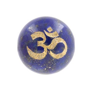 May include: A round, deep blue stone with a gold-colored Om symbol. The stone has a speckled appearance and a smooth, polished surface. The Om symbol is centered on the stone.