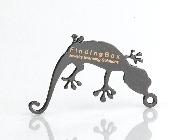 Puede incluir: Soporte de exhibici&oacute;n de joyer&iacute;a en forma de gecko de metal negro con el texto "FindingBox Jewelry Branding Solutions" grabado en el lateral.