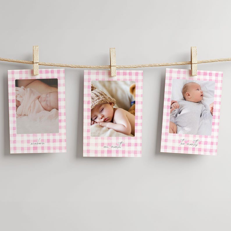 May include: Three baby milestone photo prints hanging from a string with wooden clips. Each print has a pink gingham border and a baby photo. The prints are labeled 'newborn', 'one month', and 'two months' in a script font.