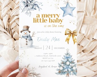May include: A festive baby shower invitation with a winter theme. The design includes a snowman, Christmas tree, and star, with the text "A merry little baby is on the way." The invitation is decorated with gold accents and blue watercolour elements.