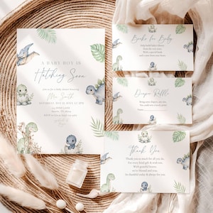 Op de afbeelding: Een set babyborrel uitnodigingen en kaarten met een dinosaurus thema. De hoofduitnodiging luidt "A Baby Boy is Hatching Soon". Extra kaarten zijn onder meer "Books for Baby", "Diaper Raffle" en "Thank You". Het ontwerp toont aquarel dinosaurussen en bladeren.