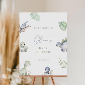 Puede incluir: Un letrero de baby shower con ilustraciones de acuarela de dinosaurios y hojas tropicales. El letrero dice "Bienvenida a la fiesta de bienvenida de Olivia" con la fecha 14 de junio de 20XX. El letrero se muestra en un caballete de cobre.