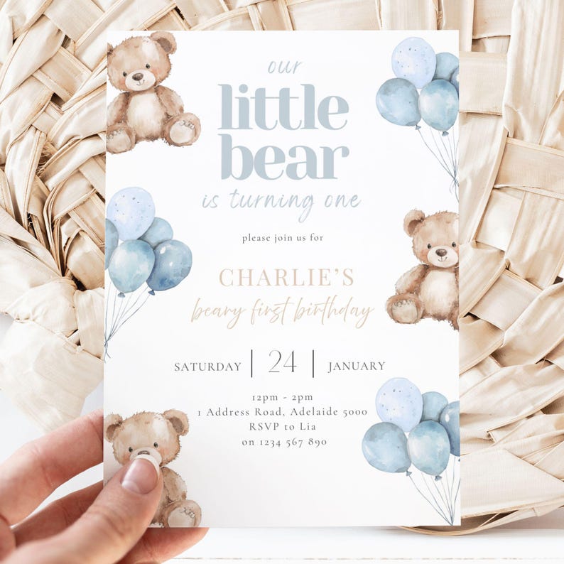 May include: A baby's first birthday invitation with a teddy bear theme. The invitation features the text "our little bear is turning one" and "Charlie's beary first birthday". It includes blue balloons and teddy bear illustrations.