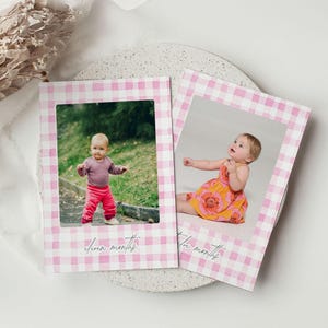 May include: Two baby photo cards with pink gingham frames. One card features a baby in a pink and white striped shirt and pink pants. The other card shows a baby in an orange floral dress. Each card has the words 'seven months' and 'three months' written in cursive.