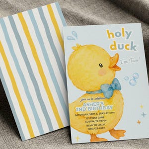 Op de afbeelding: Een verjaardagsuitnodiging met een geel aquarel eendje met een blauwe strik, de tekst "holy duck I'm Two!" en de details voor de tweede verjaardag van Asher. De kaart wordt geleverd met een bijpassende envelop met blauwe en gele strepen.