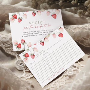 May include: Two white recipe cards with a strawberry design. The cards have the text "RECIPE for the bride to be" and lines for writing ingredients and directions. The cards are decorated with watercolor strawberries.