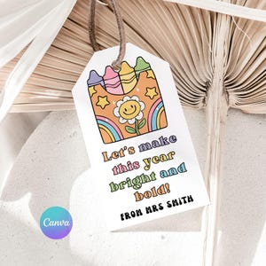 May include: A white gift tag with a brown string features a colorful illustration of crayons, a smiling flower, and a rainbow. Text on the tag reads "Let's make this year bright and bold!" and "FROM MRS SMITH."