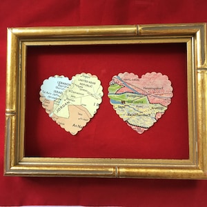 May include: Two heart-shaped maps are framed in a gold frame on a red background. The map on the left shows the Middle East, including Lebanon, Israel, Jordan, and Syria. The map on the right shows a section of Germany, including Berlin, Henningsdorf, and Reinickendorf.