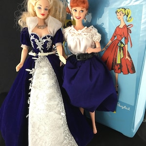 Puede incluir: Dos mu&ntilde;ecas vintage. Una mu&ntilde;eca viste un vestido de terciopelo azul con encaje blanco y una tiara plateada. La otra mu&ntilde;eca viste una blusa blanca, una falda azul y un cintur&oacute;n negro. Un archivador azul con un dibujo de una mujer con un vestido rojo est&aacute; en el fondo.