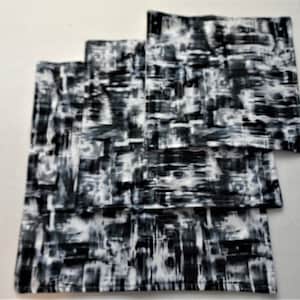 May include: Three black and white patterned fabric squares stacked on top of each other. The pattern is abstract and resembles brushstrokes.