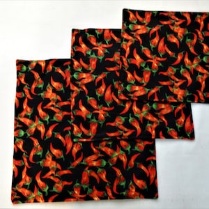 May include: Three black fabric napkins with a red chilli pepper pattern. The napkins are different sizes and are stacked on top of each other.