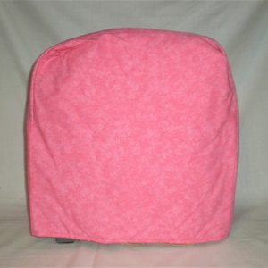May include: Pink fabric cover for a kitchen appliance. The cover has a subtle white pattern.