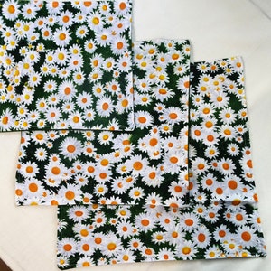 May include: Four green fabric squares with a white daisy pattern. The squares are stacked on top of each other.