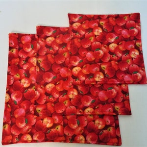 May include: Four square fabric placemats with a vibrant red apple pattern. The design features a dense arrangement of red apples with green leaves, creating a colorful and eye-catching kitchen or dining accessory.