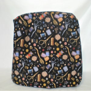 May include: A black fabric cover with a repeating pattern of sewing supplies, including spools of thread, buttons, scissors, and needles. The cover has a blue border.