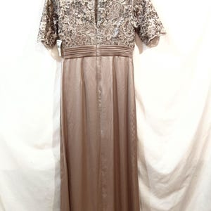 May include: A floor-length, taupe-colored dress with a lace bodice and short sleeves. The dress features a fitted waist and a flowing skirt. The back of the dress has a keyhole opening. The dress is hanging on a pink hanger.