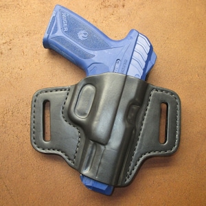 May include: A black leather holster with a blue Ruger pistol inside. The holster has a belt loop and a snap closure.