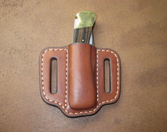 May include: A brown leather knife sheath with a white stitch detail. The sheath has a belt loop and a pocket for a knife.