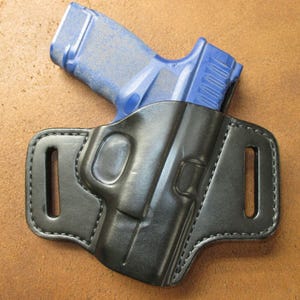May include: A black leather holster with a blue handgun inside. The holster has a belt loop and a snap closure.