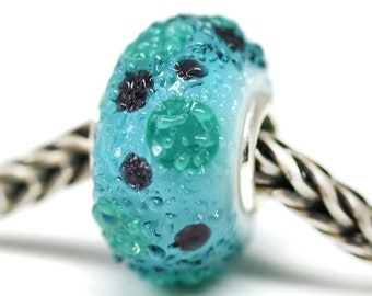 May include: A turquoise glass bead with a textured surface and a pattern of green and black dots. The bead is on a silver chain.