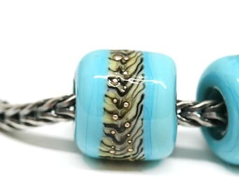 May include: A close-up of a turquoise glass bead with a gold and black patterned band. The bead is part of a bracelet with a silver chain.