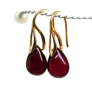 May include: A pair of gold dangle earrings with teardrop-shaped red glass stones.