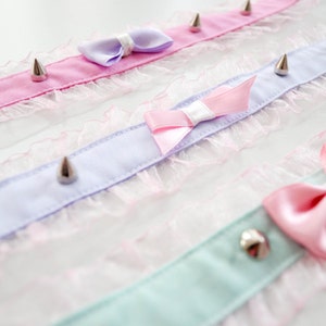 May include: Three delicate choker necklaces with lace trim and silver spikes. Each choker features a satin bow in a different pastel color: pink, lavender, and light blue.