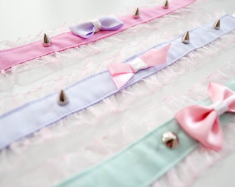 May include: Three delicate choker necklaces with lace trim and silver spikes. Each choker features a satin bow in a different pastel color: pink, lavender, and light blue.