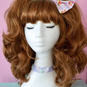 May include: A mannequin with long, curly, auburn hair wearing a lavender choker with a butterfly design. The mannequin is wearing a white bow with a pink and white floral pattern in her hair.