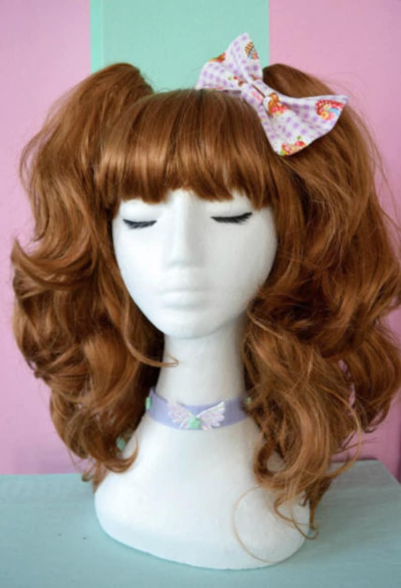May include: A mannequin with long, curly, auburn hair wearing a lavender choker with a butterfly design. The mannequin is wearing a white bow with a pink and white floral pattern in her hair.