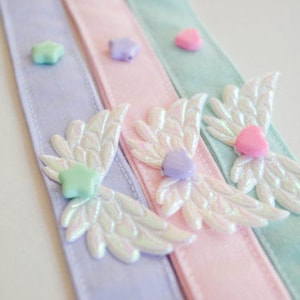 May include: Three satin ribbon hair ties with iridescent angel wings and pastel colored heart and star embellishments.