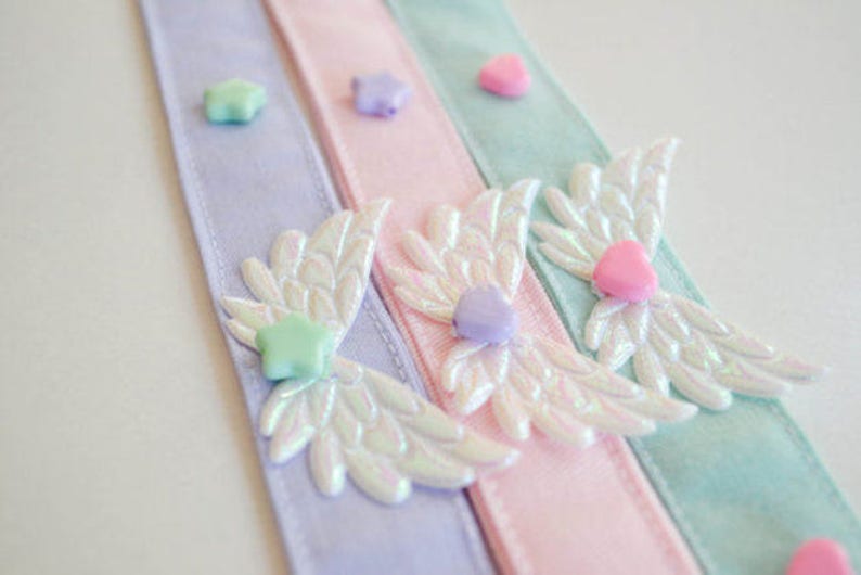 May include: Three satin ribbon hair ties with iridescent angel wings and pastel colored heart and star embellishments.