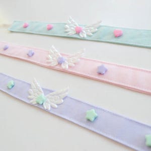 May include: Three pastel ribbon headbands with white wings and pastel colored star and heart embellishments.
