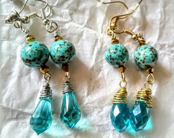 May include: A pair of turquoise and silver dangle earrings with a teardrop-shaped crystal. The earrings feature a turquoise bead with brown speckles and a silver wire wrapped around the crystal.