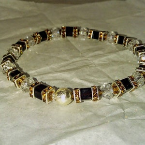 May include: A black and gold beaded bracelet with clear crystal accents and a silver charm.