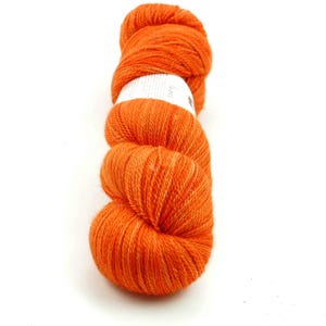 Puede incluir: Un ovillo de hilo naranja, enrollado en forma de bola. El hilo es de un color naranja brillante y vibrante.