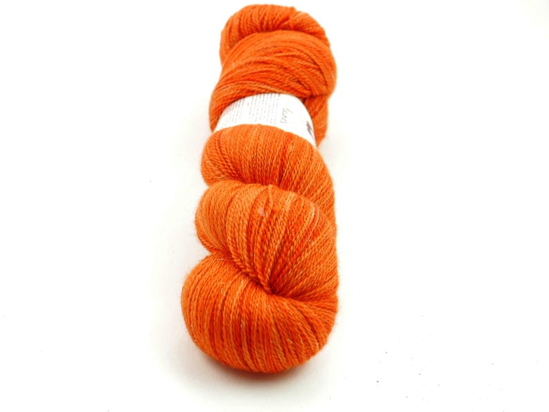 Puede incluir: Un ovillo de hilo naranja, enrollado en forma de bola. El hilo es de un color naranja brillante y vibrante.