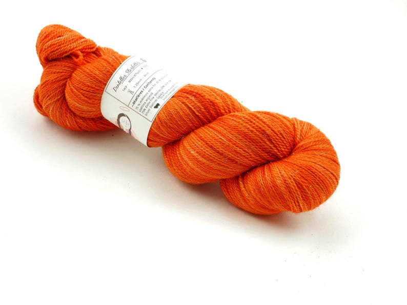 Puede incluir: Un ovillo de lana naranja con una etiqueta blanca que dice "Puddles Studio" y "Merino/Corriedale".