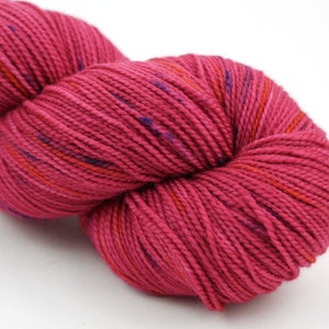 Könnte beinhalten: Eine Knäuel rosa Garn mit roten und violetten Sprenkeln. Das Garn ist weich und flauschig und perfekt zum Stricken oder Häkeln.