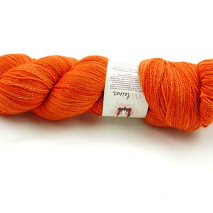 Puede incluir: Un ovillo de lana naranja con una etiqueta blanca que dice "Wool and the Gang".