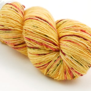 Pode incluir: Uma bola de fio amarelo com manchas vermelhas e verdes. O fio está enrolado em forma de bola.