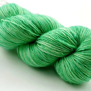 Può includere: Matassa di filato verde con riflessi bianchi. Il filato è ben avvolto e sembra morbido. Il colore è un verde vivace, primaverile, ideale per progetti di maglia o uncinetto.